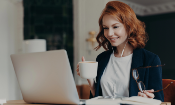 A woman with red hair holding her glasses and a cup of coffee getting ready to look for work at home jobs with A+ BBB ratings