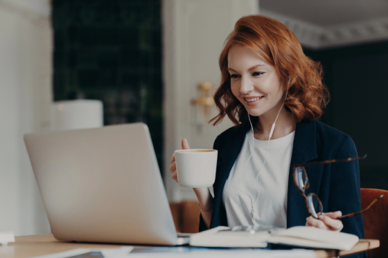 A woman with red hair holding her glasses and a cup of coffee getting ready to look for work at home jobs with A+ BBB ratings