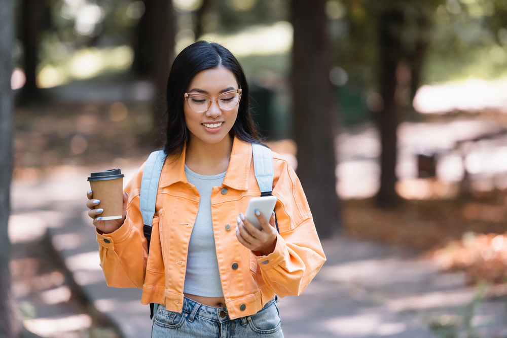 A young female drinking a coffee reading an article on her phone on hoe to get free stuff