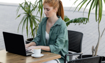 A young female with red hair using her laptop on a patio looking for online summer jobs for teachers