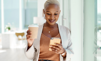 A young woman holding a to-go coffee looking for weekend jobs on her mobile phone