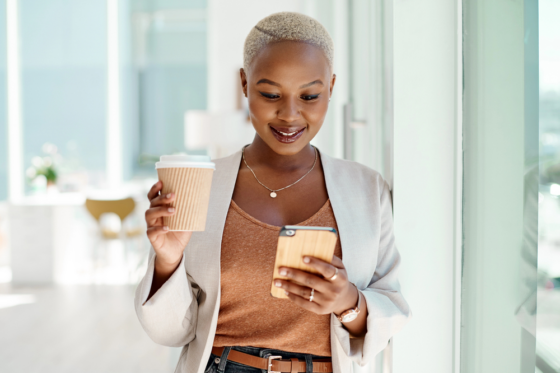 A young woman holding a to-go coffee looking for weekend jobs on her mobile phone