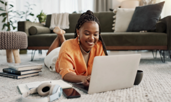 A young woman on the floor working on her laptop for the blog post make money selling your knowledge