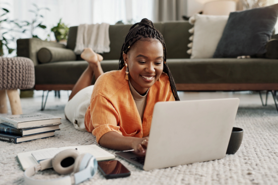 A young woman on the floor working on her laptop for the blog post make money selling your knowledge