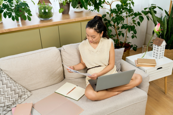 A young woman sitting criss cross on the sofa working on her laptop looking for work from home nonprofit jobs