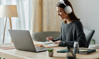 A young woman wearing headphones sitting at her desk writing something down for blog post remote jobs that pay $20 per hour