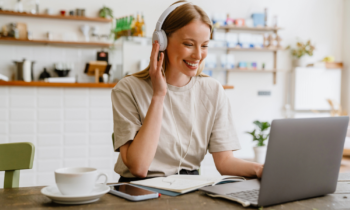 A young woman wearing headphones working in her kitchen on her laptop looking for Transcription Jobs From Home