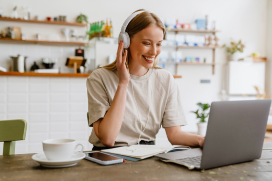 A young woman wearing headphones working in her kitchen on her laptop looking for Transcription Jobs From Home