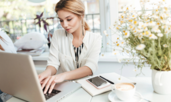 A young woman with blonde hair wearing earbuds looking for remote staffing jobs on her laptop