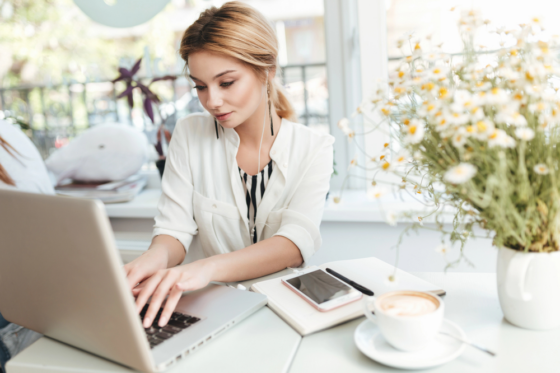 A young woman with blonde hair wearing earbuds looking for remote staffing jobs on her laptop