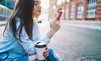 A young woman with glasses and lon hair using real apps that pay cash on her mobile device