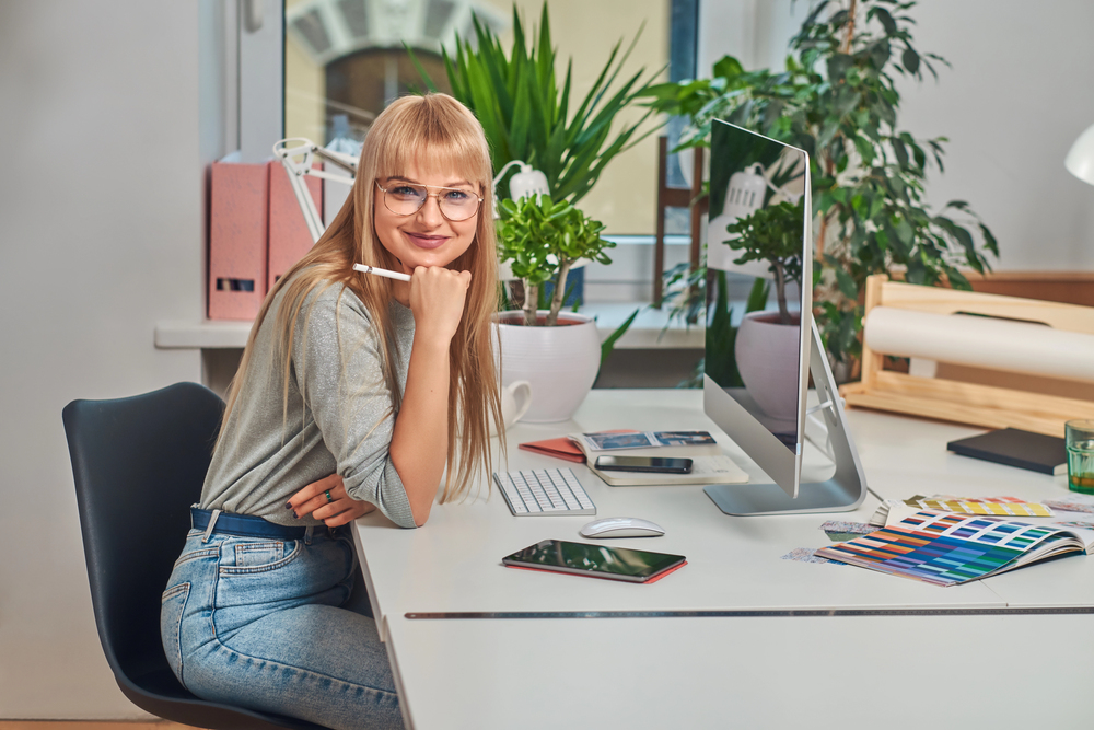 A young woman with long hair and glasses sitting at her desk getting to read an article titled best work at home jobs with Google