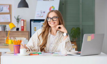 A young woman with long hair and glasses working on her laptop at home for fun work from home jobs