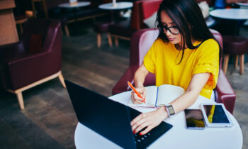 A young woman with long hair and glasses working on her laptop reading an article titled jobs you can do from home