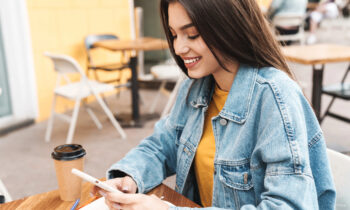 A young woman with long hair wearing a jean jacket is taking paid surveys on her phone
