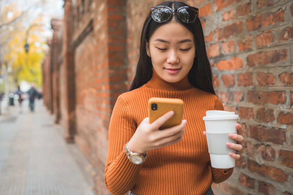 A young woman with sunglasses on her head looking at her mobile phone reading an article titled apps that pay real cash