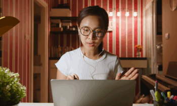 An Asian woman wearing glasses working from home on her laptop during night hours