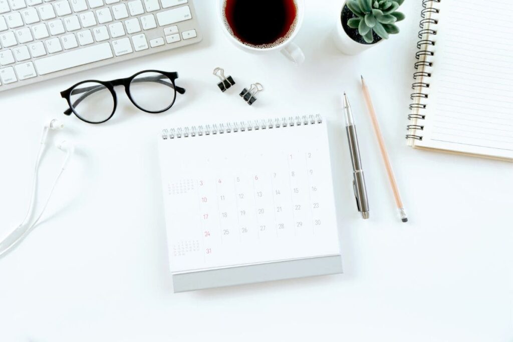 A home office desk, with a keyboard, calendar, cup of coffee, and a plant.