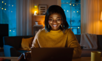 Beautiful Smiling Black Girl Working on a Laptop while Sitting at Her Desk at Home. In the Evening Creative Woman Works on a Computer at night