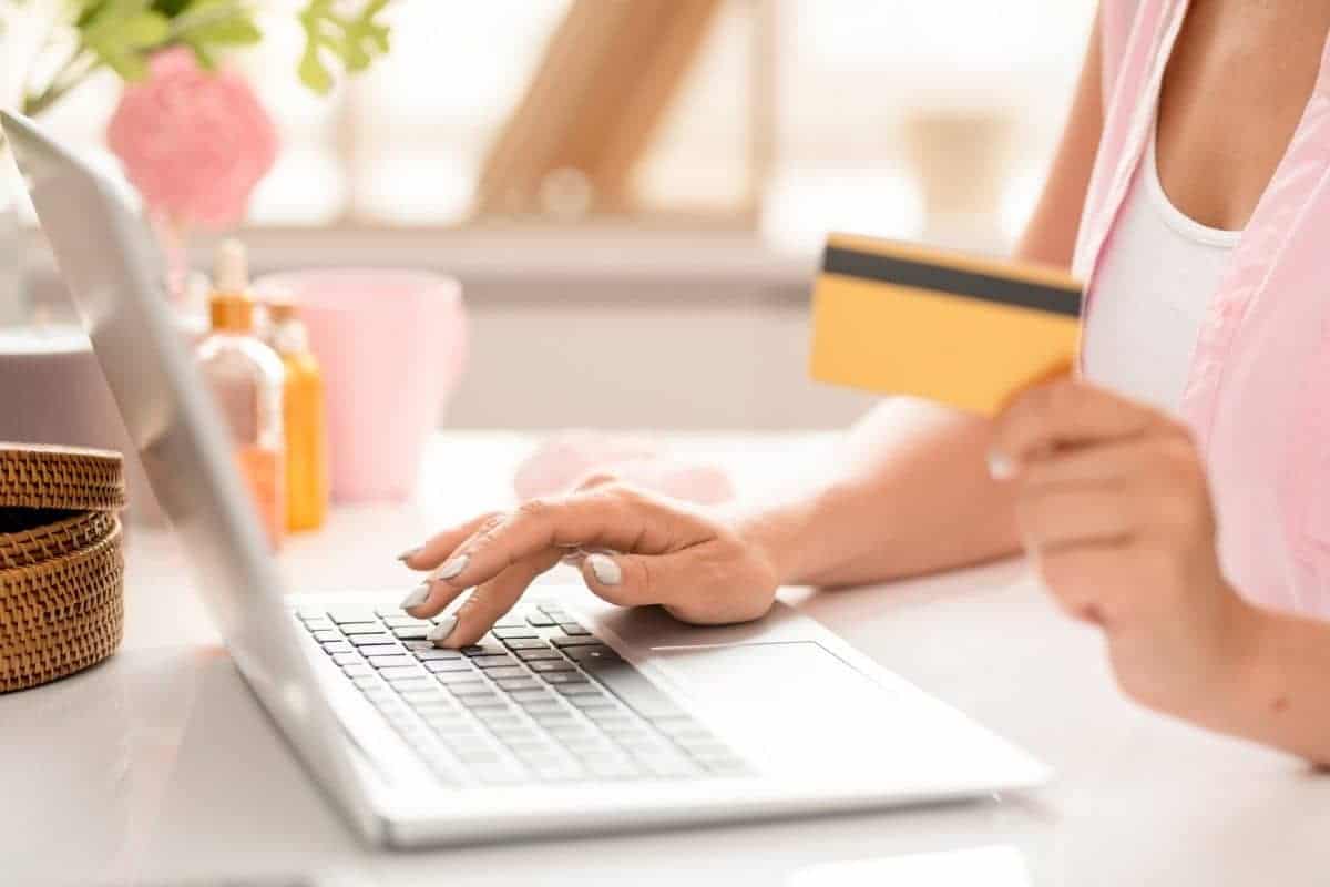 A closeup image of a woman sitting at a desk, shopping online, using a coupon site, and holding a credit card.