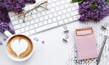 Overview of a keyboard, latte, a pad of paper sitting next to purple flowers for Christian remote jobs