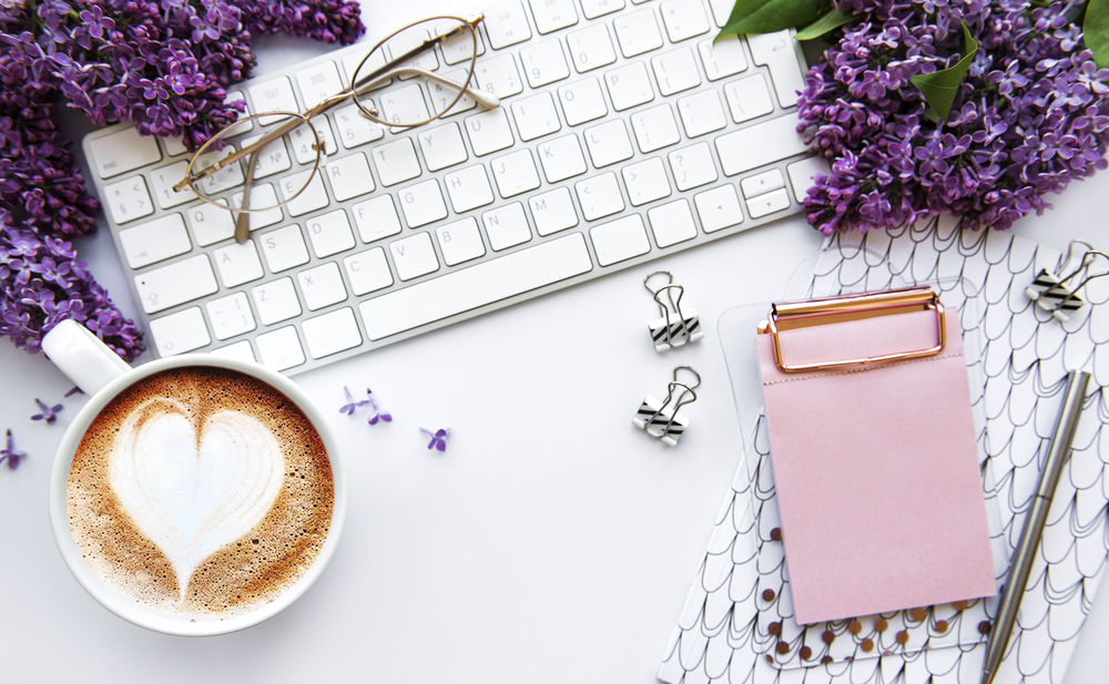 Overview of a keyboard, latte, a pad of paper sitting next to purple flowers for Christian remote jobs