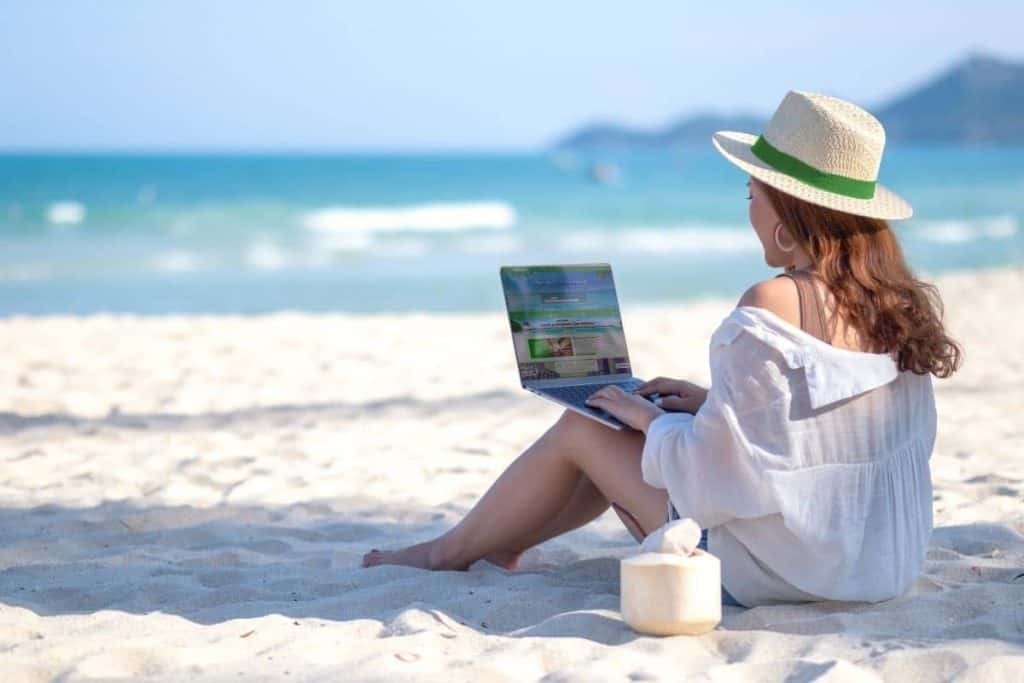 Cruise Planners franchise owner works as a travel agent from the beach on her laptop.