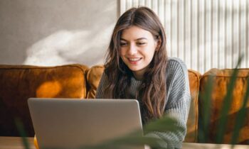 Woman working from home on a couch, using a laptop.