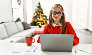 Young woman with long hair sitting at desk working on computer with Christmas free in the background