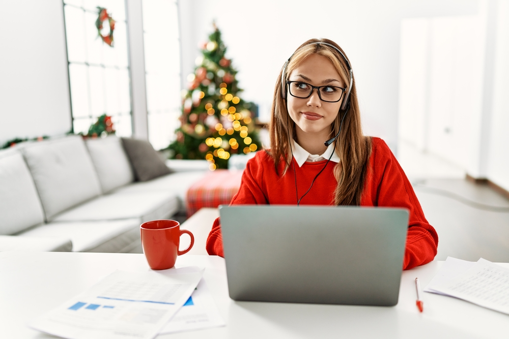 Young woman with long hair sitting at desk working on computer with Christmas free in the background