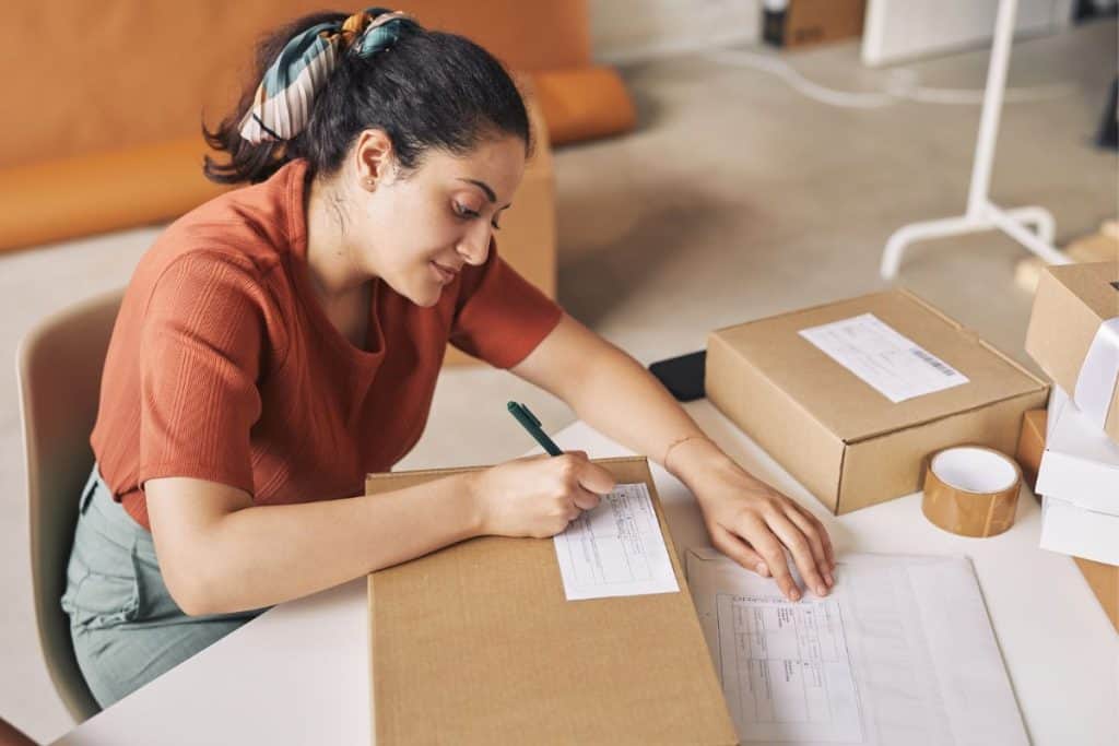 A woman online seller, writing on a shipping package label.