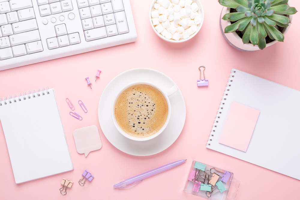 feminine office space with keyboard, plant, notebook, pens, and a latte