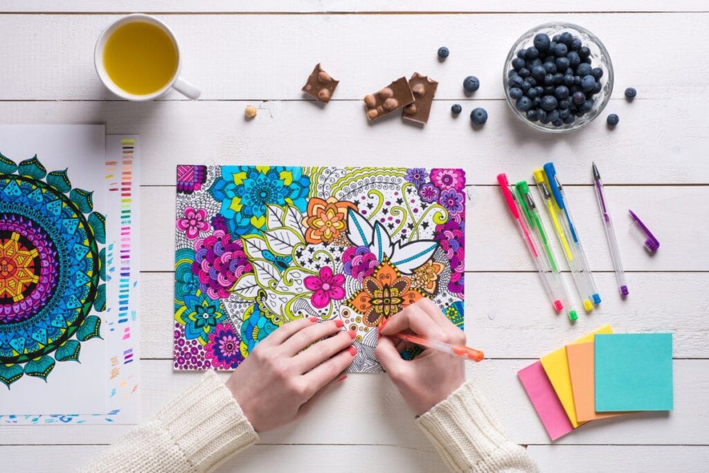 Overhead view of a woman using colored pencils coloring designs in adult coloring book.