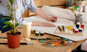A closeup view of an artist's desk: a woman is using paints to color a large canvas.