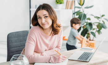 young mom working on computer with son playing in the background