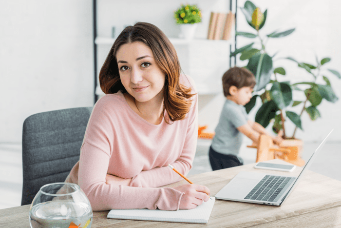 young mom working on computer with son playing in the background