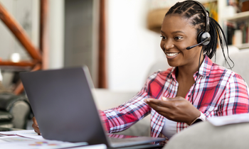 Happy positive smiling young black woman in casual outfit providing remote customer service for blog post TTEC jobs work from home