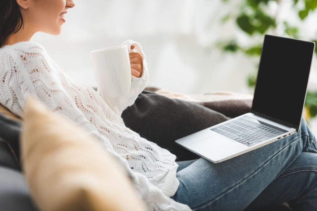 A woman working from home, drinking a cup of coffee while she uses her laptop.