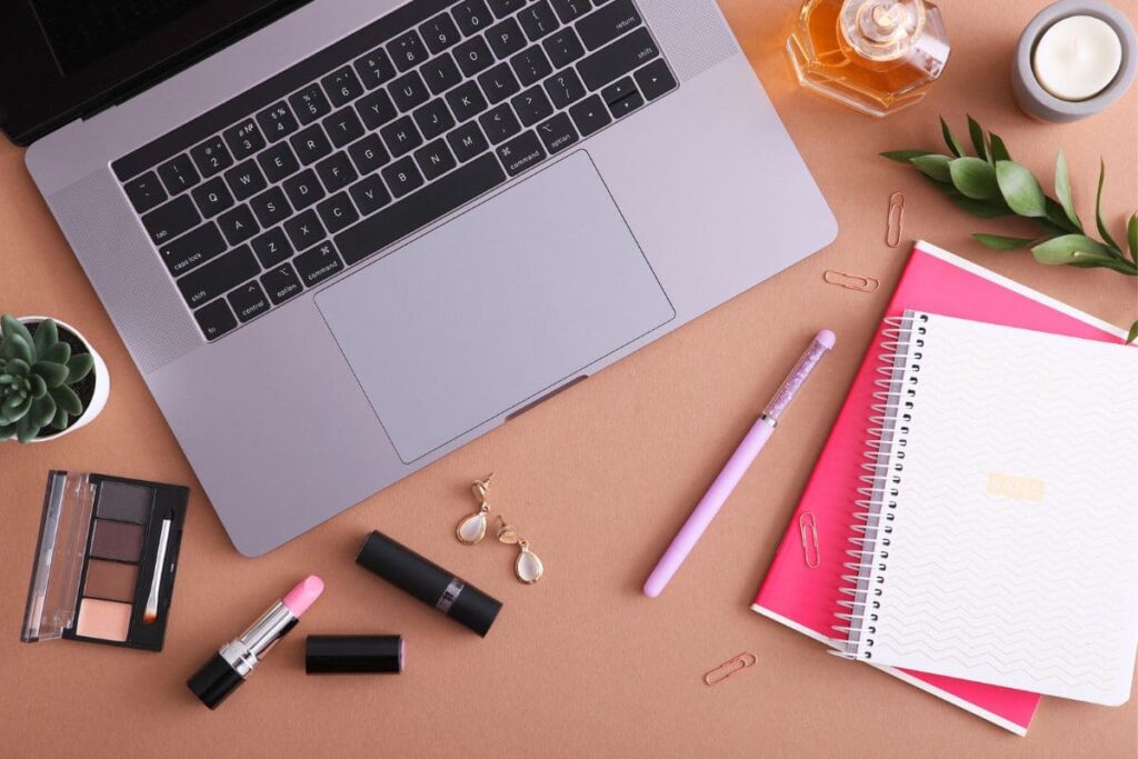 A content creator's home office desk, with a laptop, cosmetics, and a notebook.