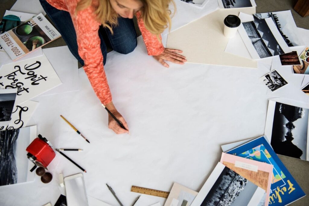 He is working on a floor vision board, drawing on a large poster board, with magazine cuttings and collage items drawn in the background.