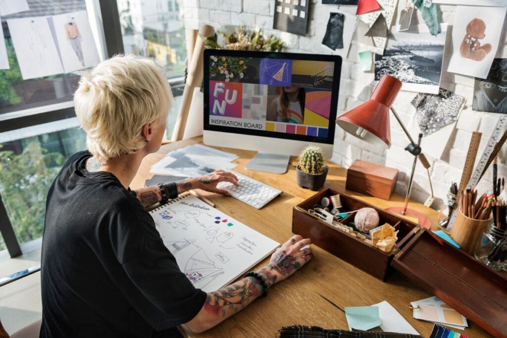 Woman working at home office desk with vision board in the background.
