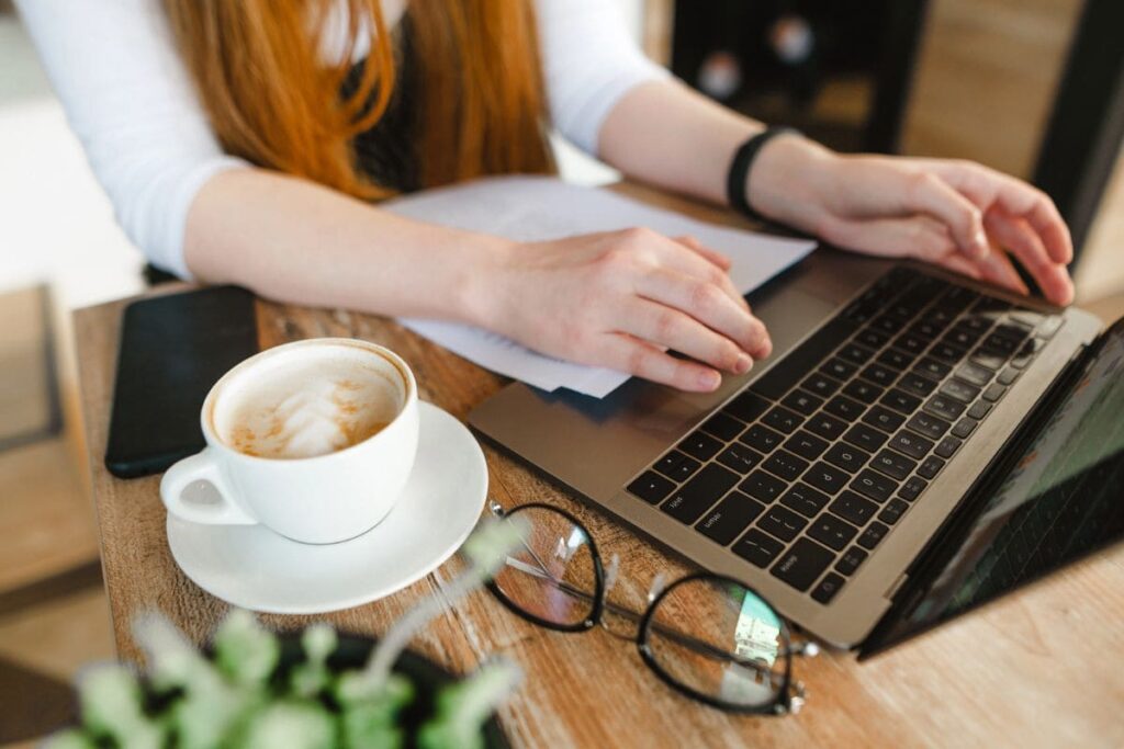 A woman working remotely in a cafe, using a laptop and drinking coffee.