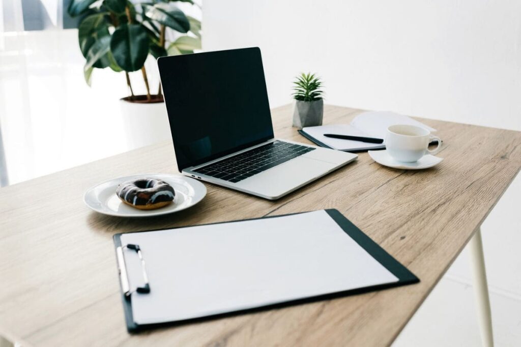 A clipboard, laptop, plant, and a cup of coffee sitting on a remote worker's home office desk in preparation for an interview.