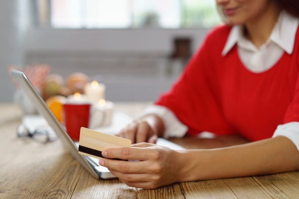 A woman sitting at a kitchen table, using a laptop and holding a free Target giftcard.