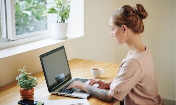 A woman working from her home office desk, using a laptop and writing in a notebook for blog post get hired without experience