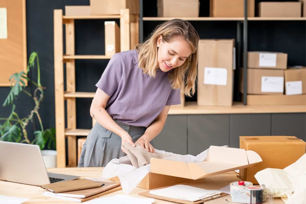A woman in her home office, packing products into shipping boxes.
