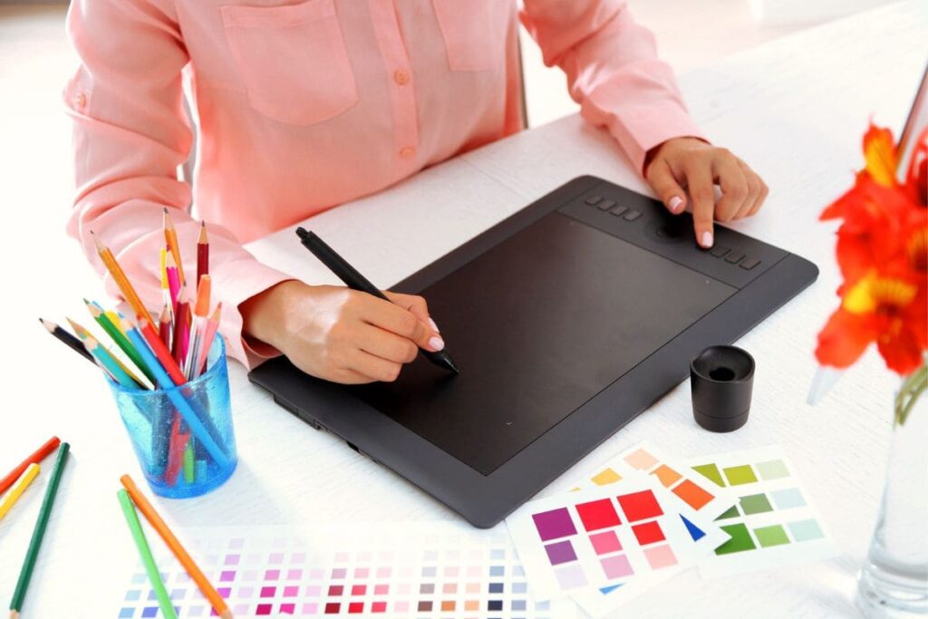 A graphic designer sitting a desk, using a drawing tablet, surrounded by design tools and art supplies.