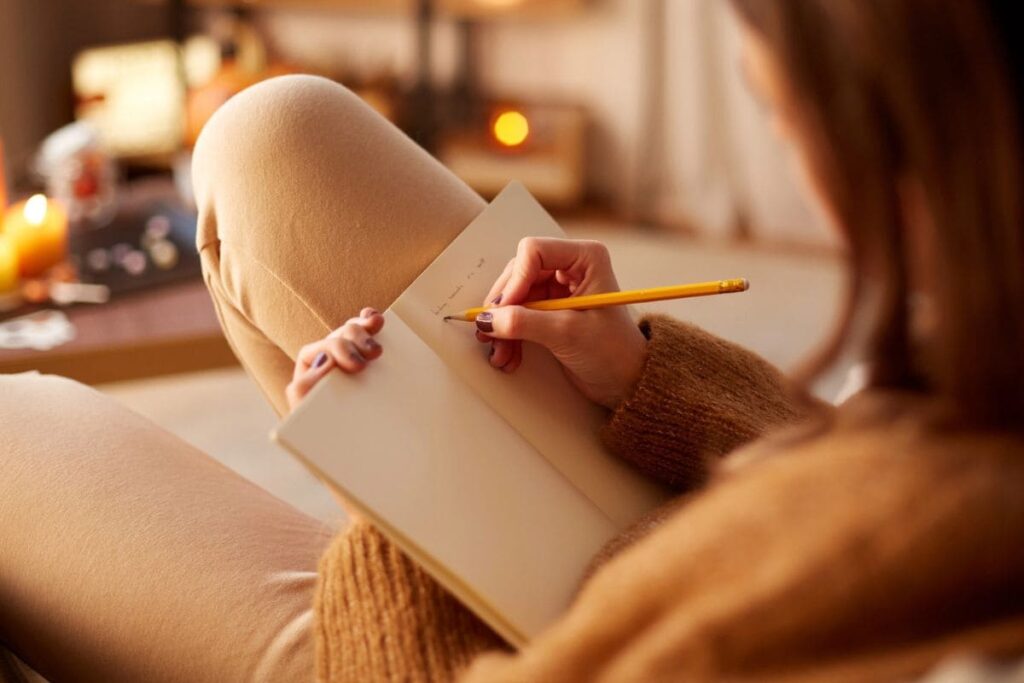 A cozy closeup image of a woman sitting on the couch, writing in a notebook.