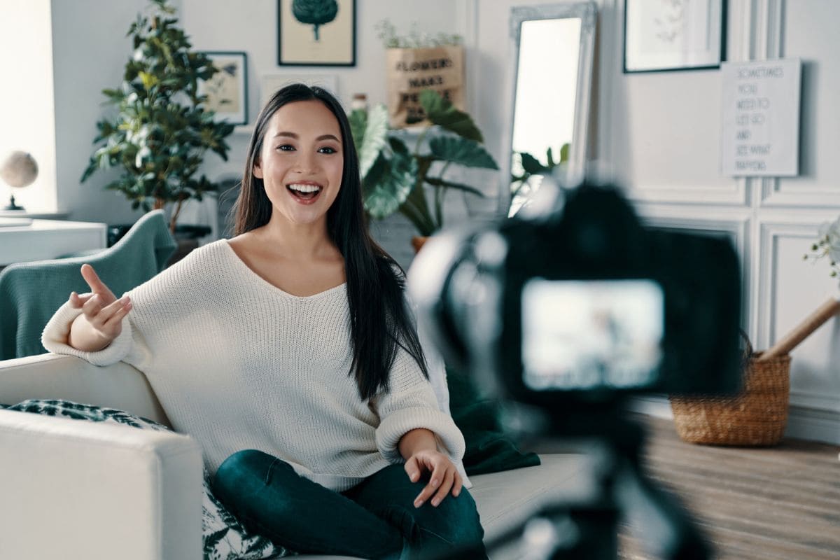 A content creator sitting in her living room, filming a video using a DSLR camera.