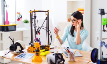 A woman using a 3d printer at her home office desk.